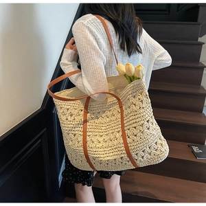 Detailed hollow crochet straw tote bag with brown leather straps shown on shoulder