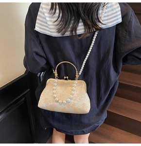 Detail of vintage jacquard crossbody bag with gold metal handle and pearl strap on model