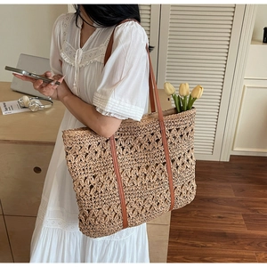 Detail of hollow woven straw tote bag with brown leather straps worn on shoulder