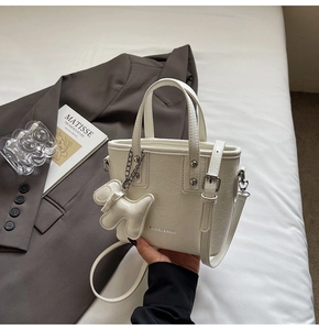 Chic cream white bucket bag with pebble texture and cute puppy charm on white bedding