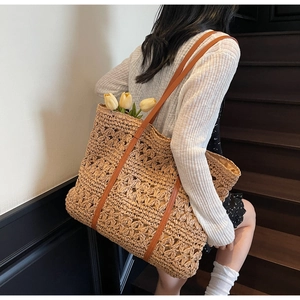 Detail view of hollow straw tote bag with brown leather straps on a wooden staircase