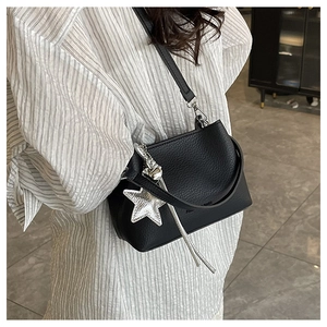 Détail du sac seau noir à motif litchi avec breloque étoile porté par un mannequin