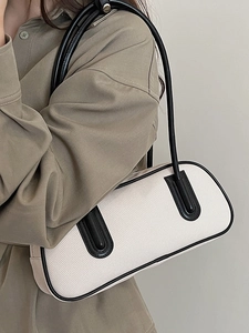 Minimalist cream canvas bowling bag with black leather trim shown in a shoulder carry pose