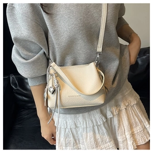 Gros plan du sac seau minimaliste en cuir crème avec breloque cœur argentée et gland