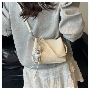 Détail du sac seau en cuir crème avec pendentif étoile et décoration de pompons