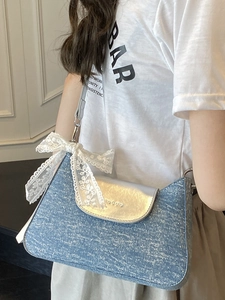 Blue denim crossbody bag with silver lid and lace bow charm shown on a model