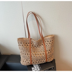 Detail of hollow floral straw weaving and brown leather shoulder strap on tote bag