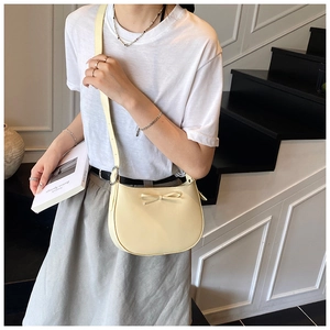 Détail du sac à bandoulière beige crème avec nœud décoratif porté par un modèle