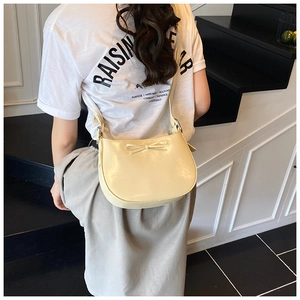 Gros plan d'un sac à bandoulière crème avec nœud papillon en cuir verni brillant