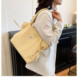 Détail du sac cabas plissé jaune avec nœud coulissant et étiquette sur costume blanc