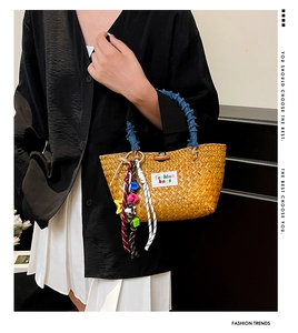 Detail of woven straw handbag featuring blue denim handles and colorful fashion charms