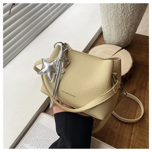 Détail du sac seau en cuir grainé jaune clair avec des breloques étoile et cœur argentées