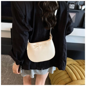 Vue détaillée d'un sac demi-lune crème avec nœud papillon porté par un mannequin