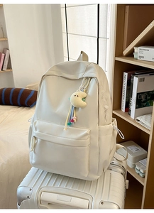 Detail eines cremeweißen Rucksacks mit Mond-Plüschanhänger auf weißem Koffer