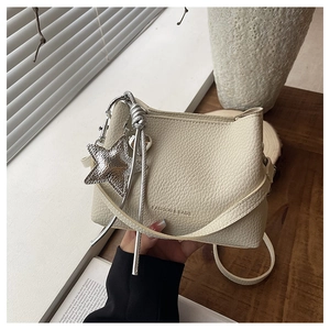Détail d'un sac seau beige à motif litchi avec breloque étoile argentée et bandoulière