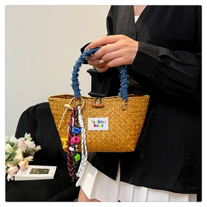 Detail of straw handbag featuring denim handle, colorful charms and wooden button closure