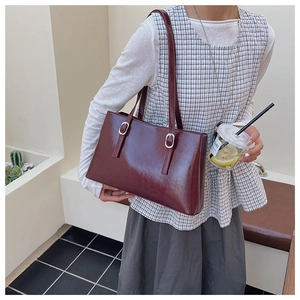 Side view of a wine red tote bag with silver square buckles and glossy finish