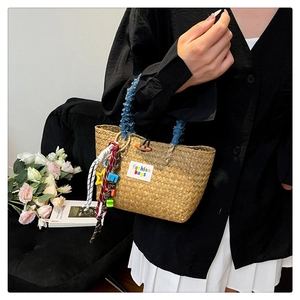 Detail of hand-woven straw tote bag with denim handle and colorful fashion charms