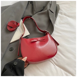Détail du sac croissant rouge brillant avec nœud et bandoulière amovible