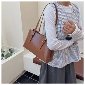 Detailed view of brown PU leather tote bag with silver buckles worn by a model