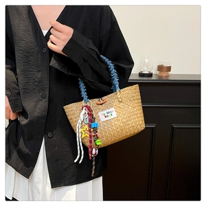 Detail of hand-woven straw beach bag with blue plush handle and colorful star pendants
