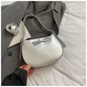 Détail d'un sac demi-lune argenté avec nœud décoratif et ceinture fine assortie