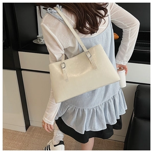 Detail of cream white faux leather tote bag showing glossy texture and silver buckle