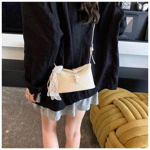Détail d'un sac seau en cuir tressé crème avec nœud en dentelle et breloque perle