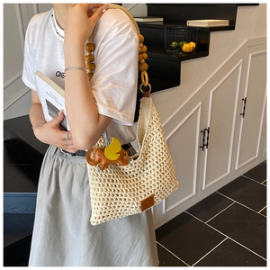 Detail of hand-woven beige beach bag with wooden bead straps and elephant charm