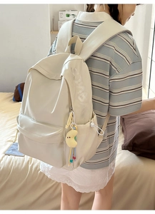 Detail des cremeweißen Rucksacks mit Buchstabenprägung und Plüsch-Mond-Schlüsselanhänger