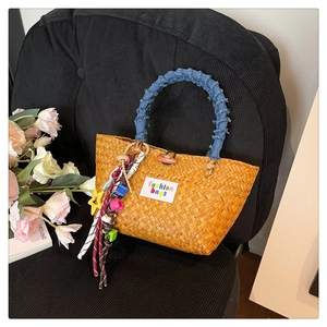 Detailed shot of an orange woven straw bag with denim handles and a colorful bead charm