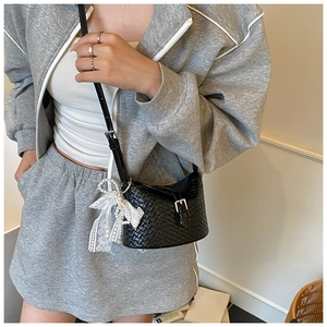Détail d'un sac bandoulière noir texturé avec nœud en dentelle porté par un mannequin