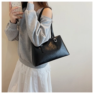 Detail of glossy black tote bag with silver metal buckle on a shoulder strap for women