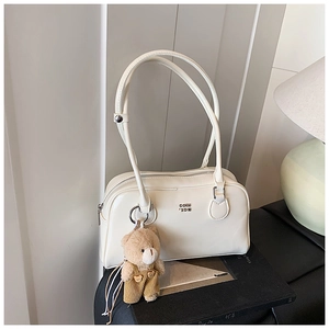 Détail d'un sac à main blanc minimaliste avec logo doré et charm d'ours en peluche