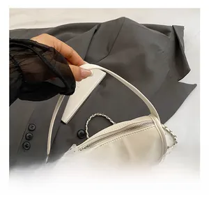 Detail of cream-white handbag with zipper closure and woven metal chain strap on gray suit