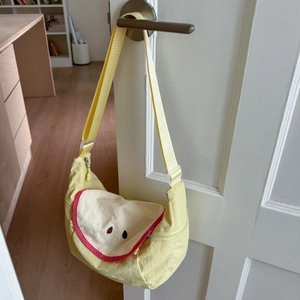 Detail of light yellow crescent shoulder bag with red trim hanging on a white door handle