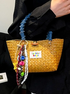 Handwoven straw basket bag with denim-wrapped handle and colorful charms for beach vacation