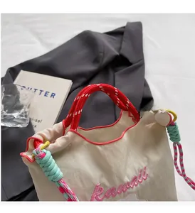Dettaglio borsa a secchiello crema con manici intrecciati rossi e ricamo kawaii