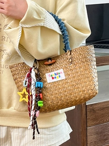 Handwoven straw bucket bag with blue pleated handles and colorful letter charms for beach