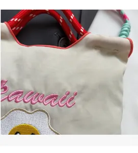 Dettaglio della borsa in nylon crema con ricamo Hawaii rosa e motivo smiley a uovo