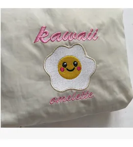 Dettaglio del ricamo di un simpatico uovo al tegamino con scritta kawaii su tessuto beige