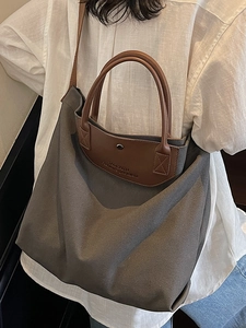 Large gray canvas tote bag with brown leather handles worn by a model in white linen
