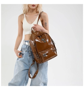Brown patent leather punk backpack featuring metallic cross hardware and ring details on model
