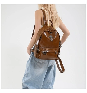 Detail of a shiny dark brown punk backpack with silver metal cross and ring accents