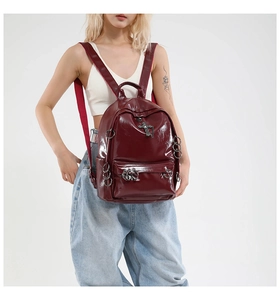 Detail of burgundy glossy leather punk backpack with silver cross charm and metal rings