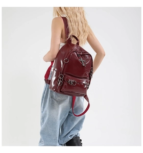 Detail view of burgundy glossy backpack featuring punk metal rings and cross pendant accessory