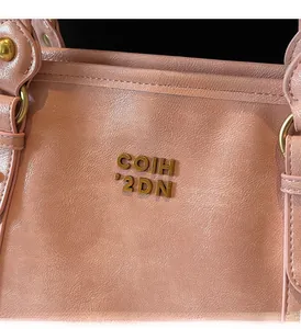 Detail der rosa Ledertasche mit Metallic-Logo und glänzender, strukturierter Oberfläche