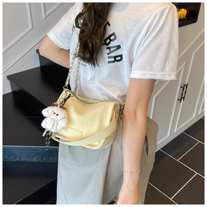 Close-up of a cream pleated underarm bag with a plush dog pendant and chain strap