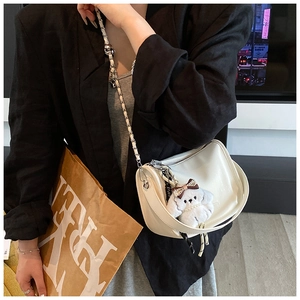 Detail of white glossy moon bag with plush dog charm and silver chain strap