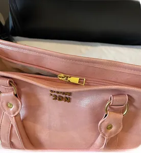 Detailaufnahme des glatten Goldreißverschlusses und der Metallbuchstaben auf der rosa Tasche